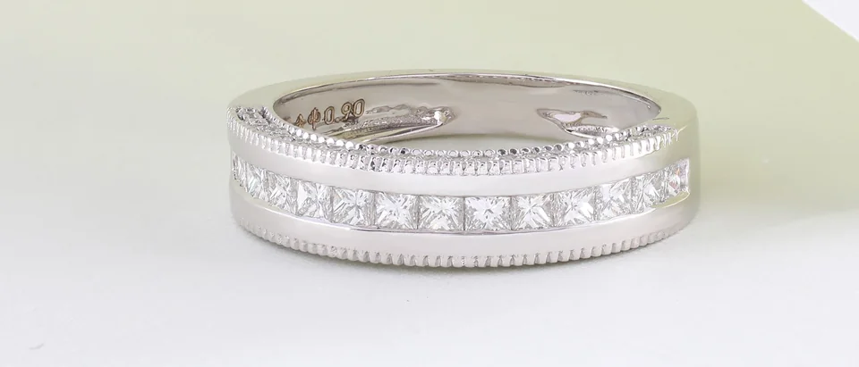 A white gold band set with a channel of square diamonds on a pale surface