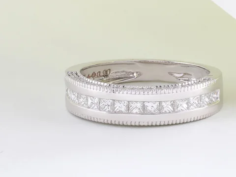 A white gold band set with a channel of square diamonds on a pale surface