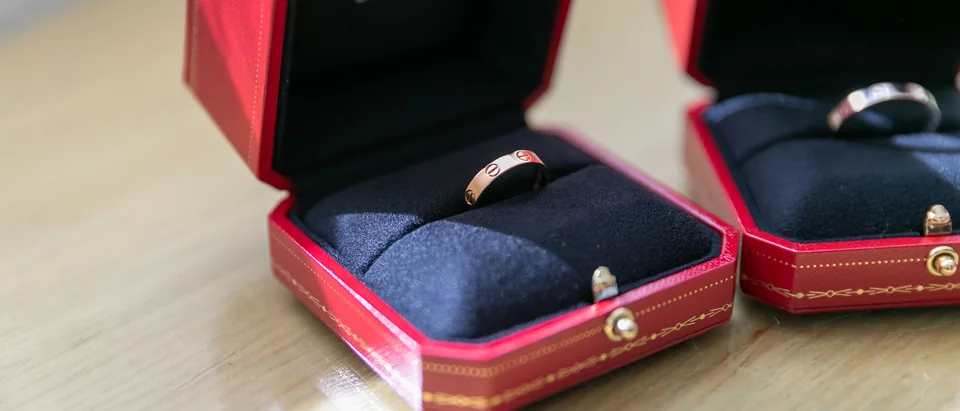 Two gold bands in open red Cartier ring boxes on a pale wooden table