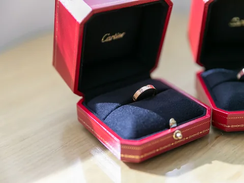 Two gold bands in open red Cartier ring boxes on a pale wooden table