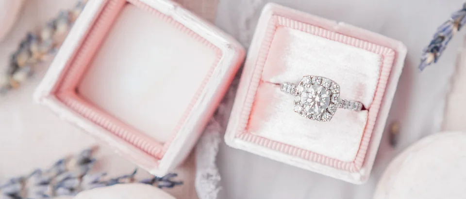 A cluster diamond ring in an open pink ring box among pale macarons and lavender