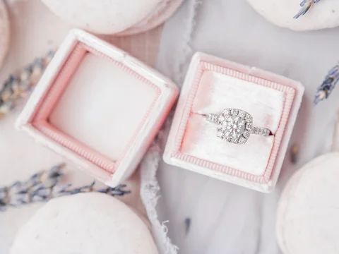 A cluster diamond ring in an open pink ring box among pale macarons and lavender