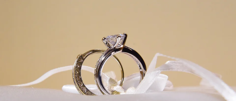 A solitaire engagement ring and a band tied to a white satin ring pillow