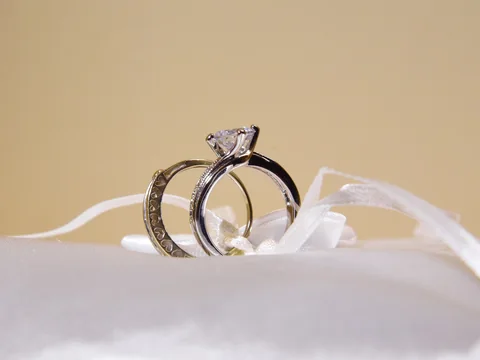 A solitaire engagement ring and a band tied to a white satin ring pillow