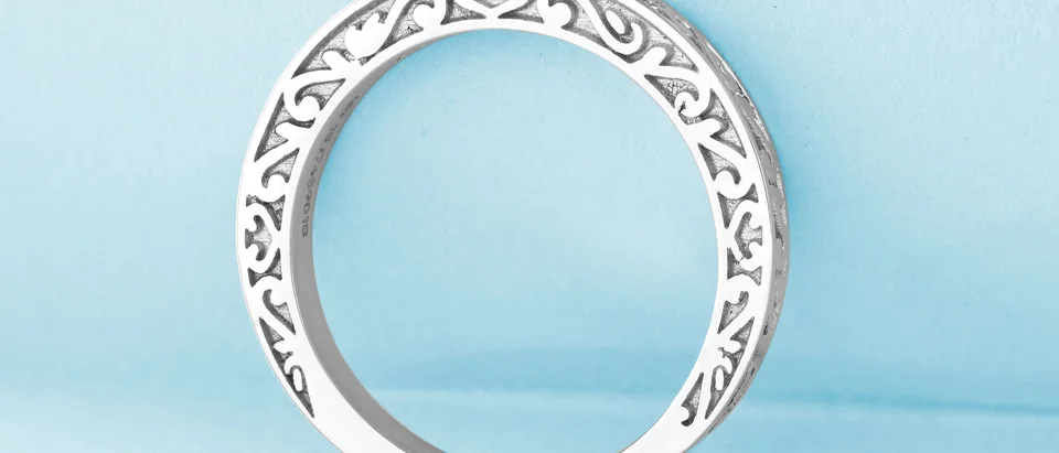 A white gold band with an open scroll pattern standing on a pale blue ground