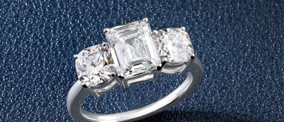 A three-stone ring with an emerald-cut center diamond on dark blue leather