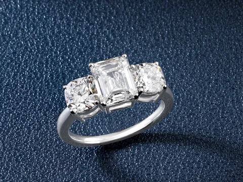 A three-stone ring with an emerald-cut center diamond on dark blue leather