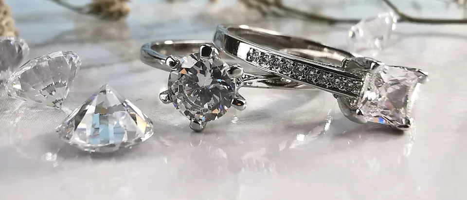 Diamond rings and loose stones on white marble under dried flowers