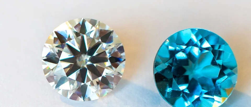 A round brilliant diamond beside a round blue gemstone on a white surface