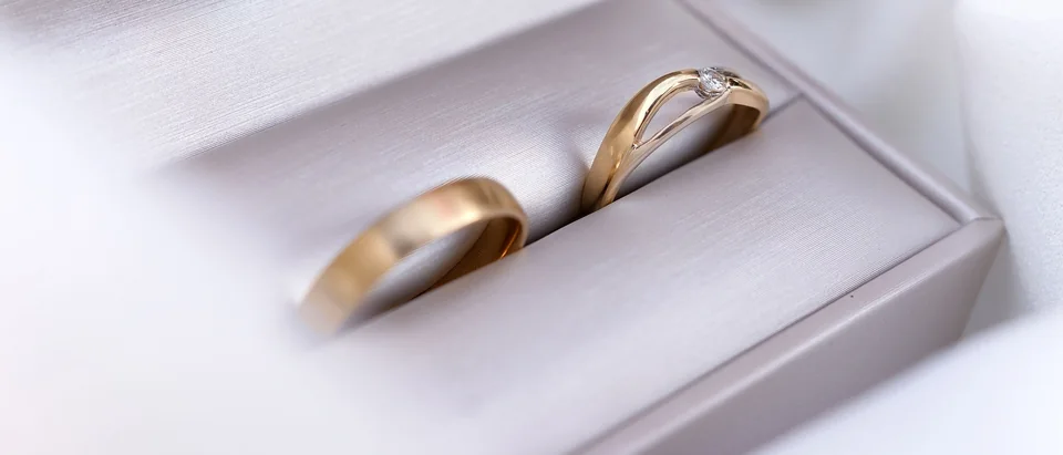 Two gold wedding bands, one set with a small diamond, in an open white ring box