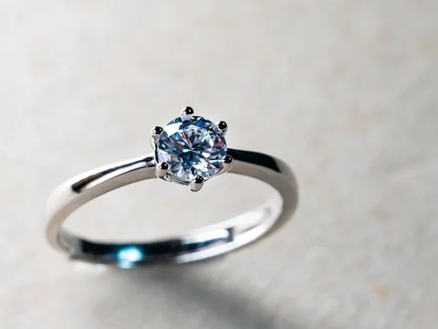 A six-prong solitaire diamond ring in white gold on pale textured paper
