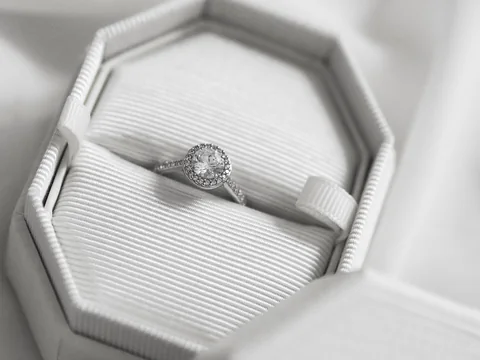 A diamond ring in an open white octagonal ring box on white fabric