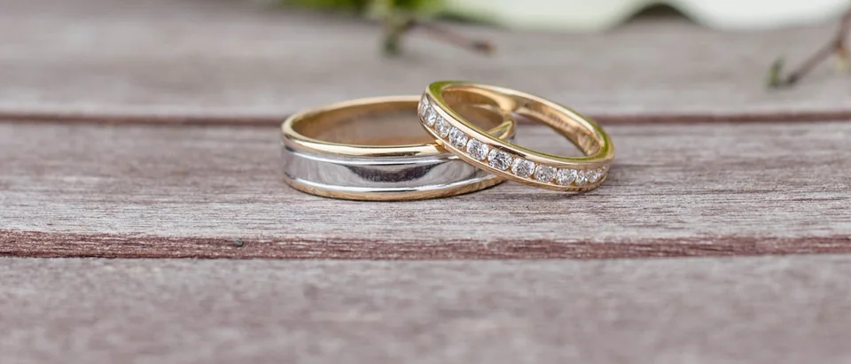 Two wedding bands, one set with diamonds, on pale wooden boards