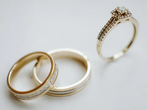 A diamond engagement ring beside two gold wedding bands on a pale gray ground