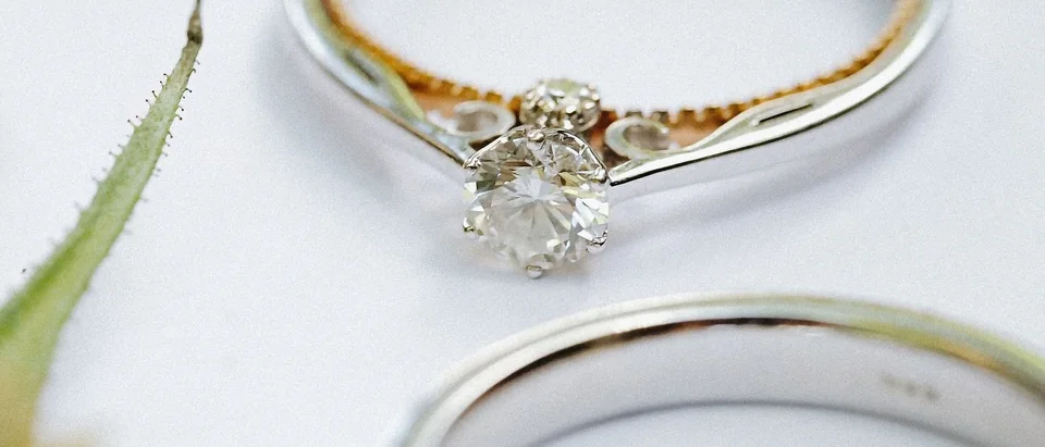 A solitaire diamond ring between two white gold bands on a white surface